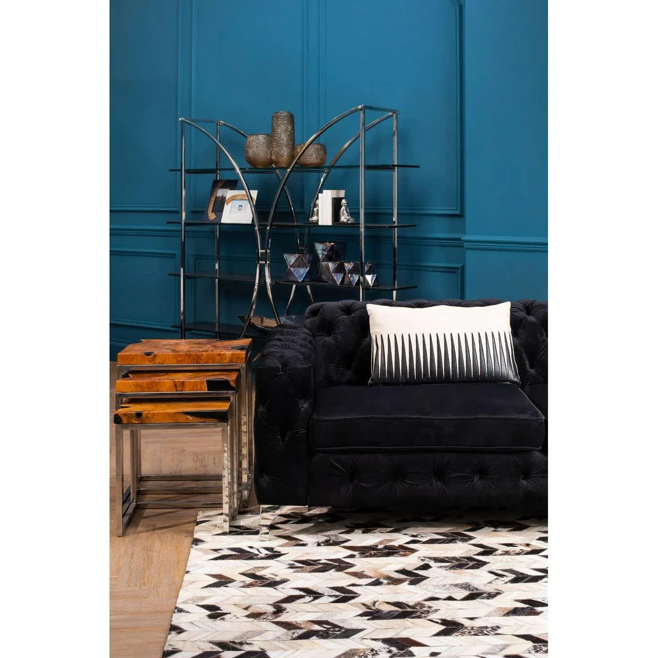 Modern black velvet sofa with cushion, geometric rug, and wooden nesting tables in living room