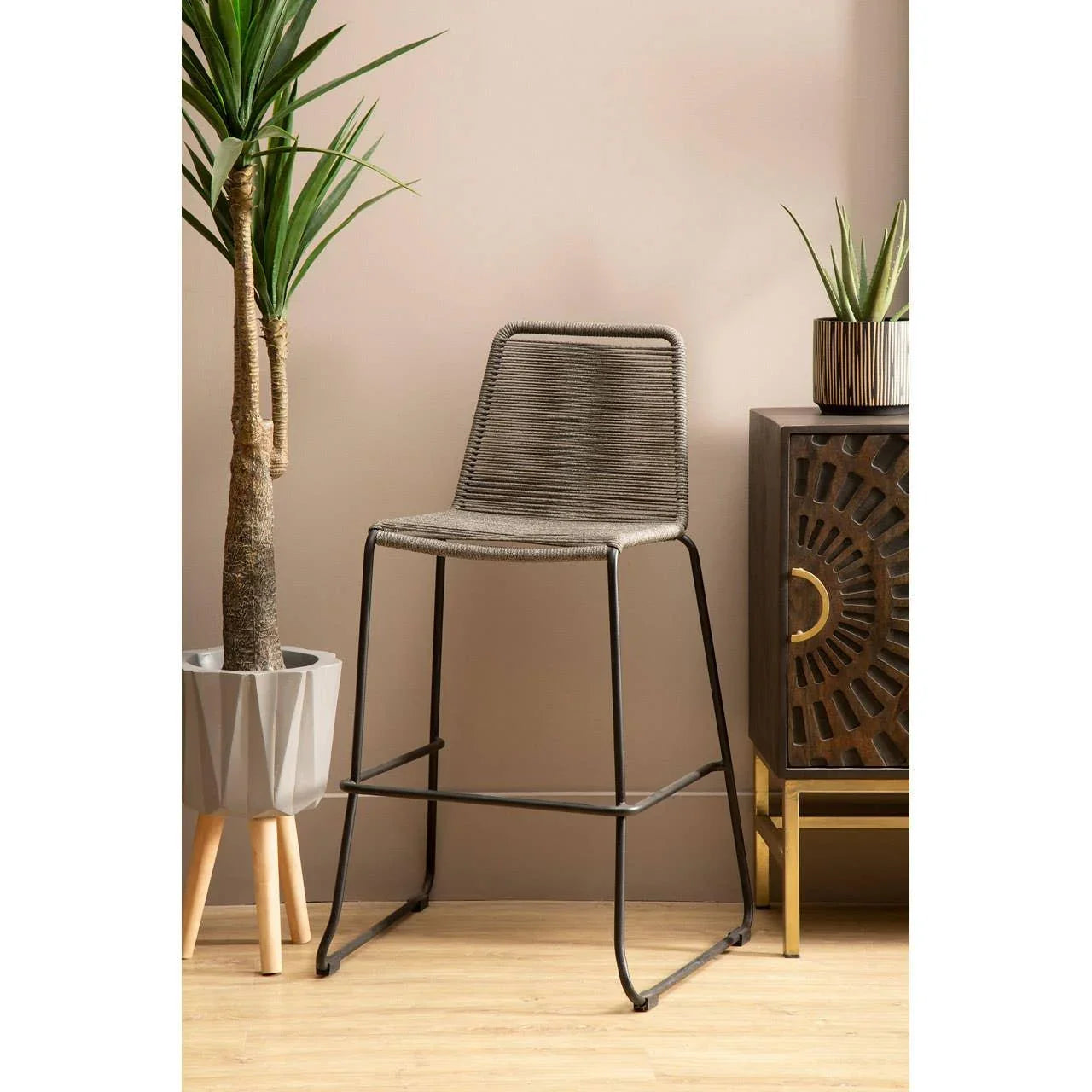Grey woven bar stool with metal legs beside indoor plant and dark wood sideboard