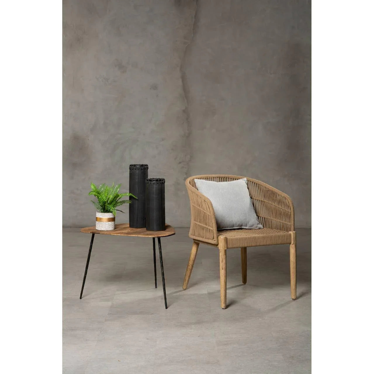 Rattan accent chair with grey cushion next to wooden side table with vases and potted plant