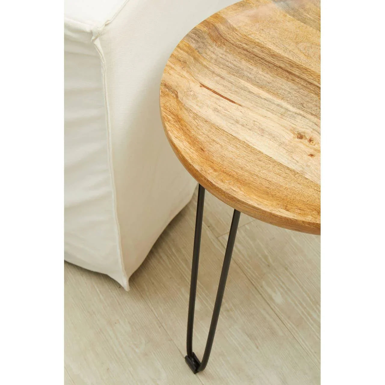Round wooden side table with metal legs beside cream fabric sofa on light wood floor