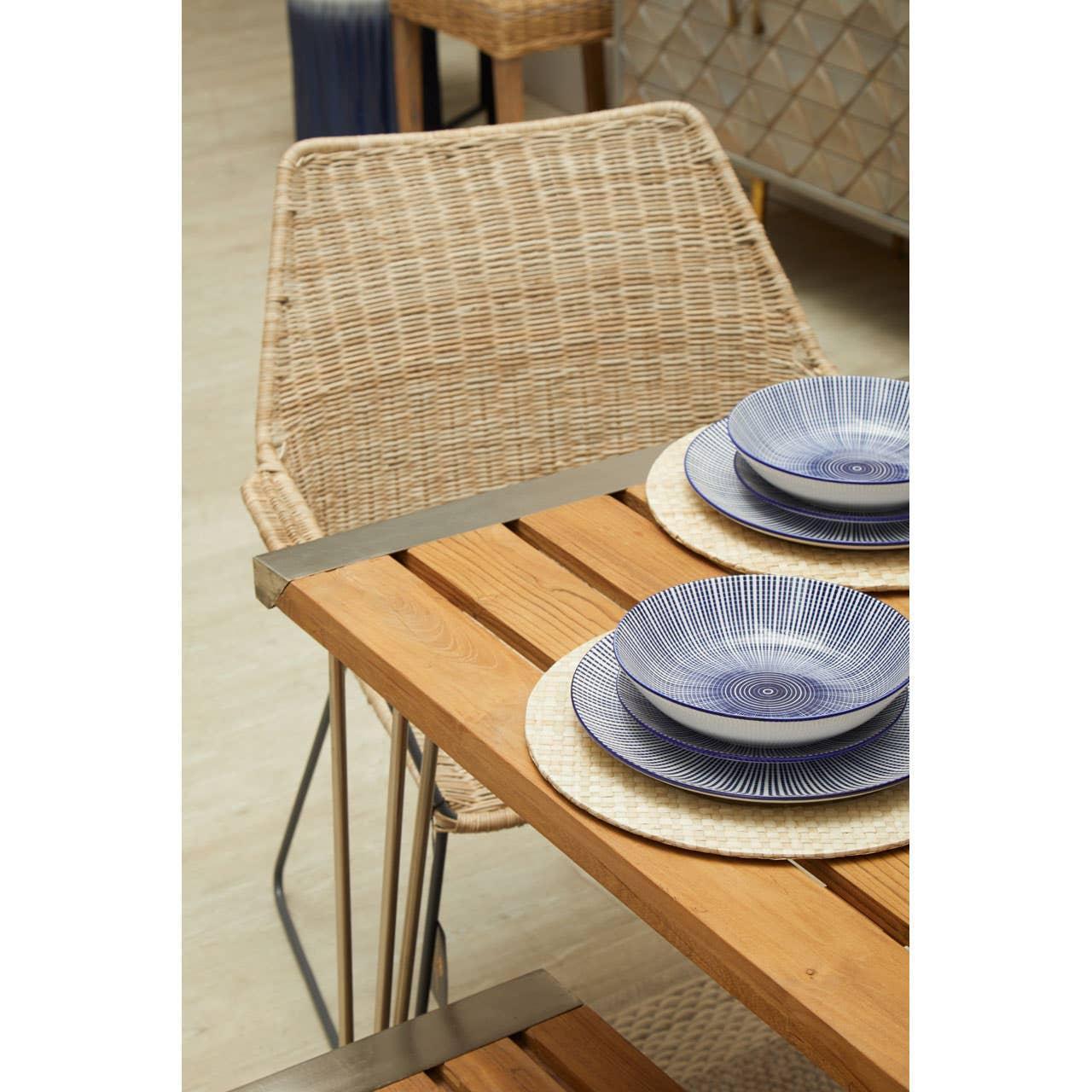 Wooden dining table with woven chair and blue patterned dinnerware set on placemats