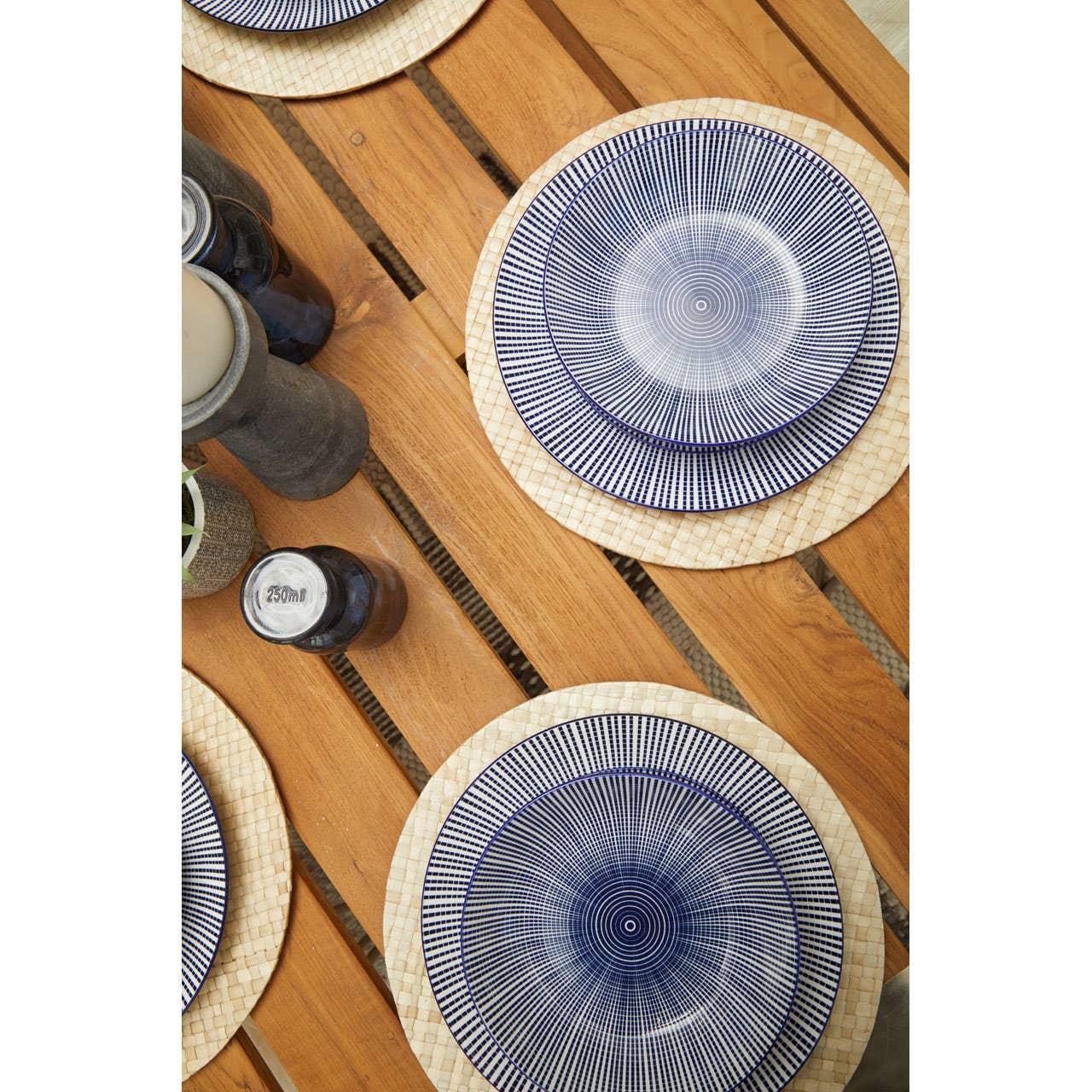 Outdoor wooden dining table with patterned blue ceramic plates and woven placemats