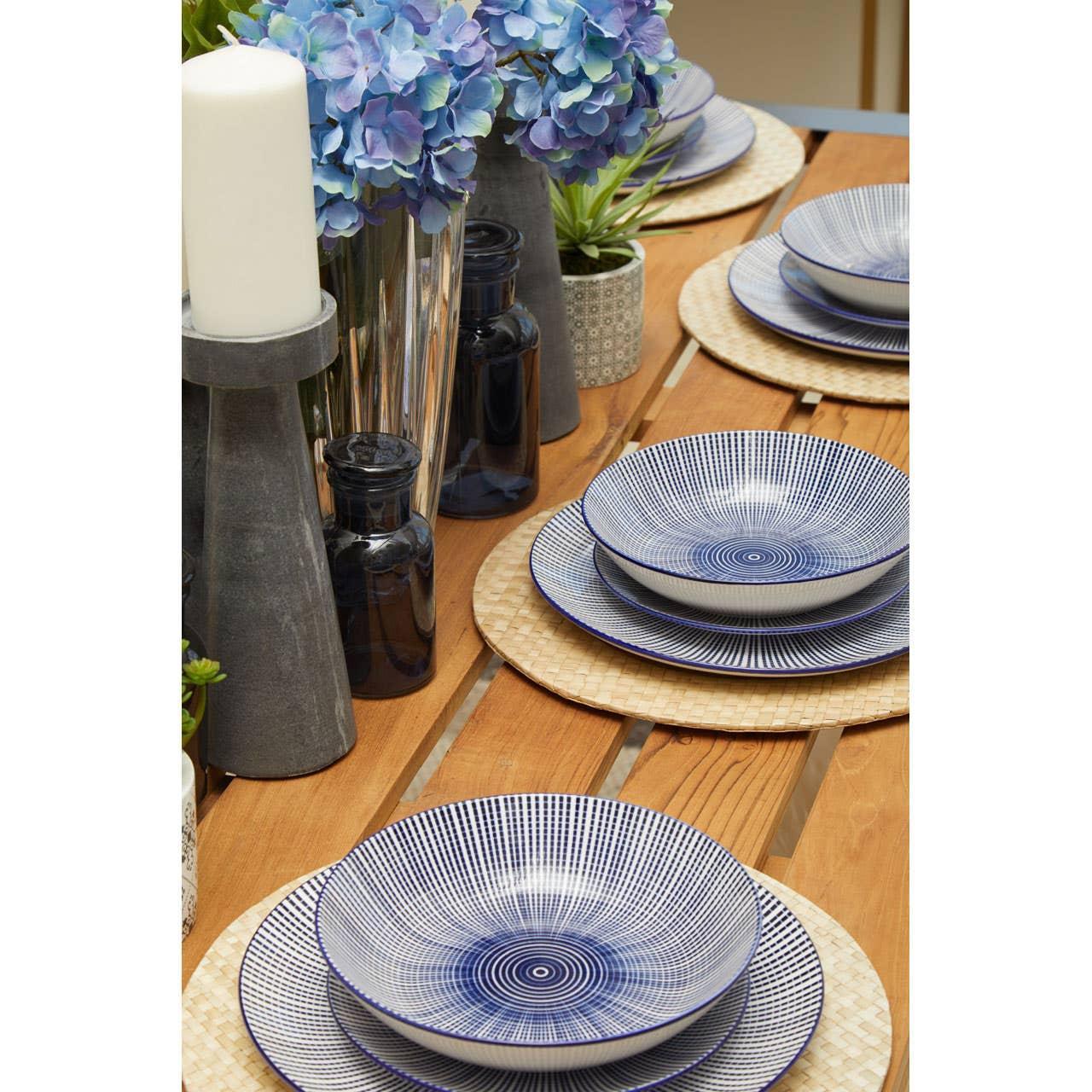 Blue patterned dinnerware set on wooden dining table with placemats, candles and flowers
