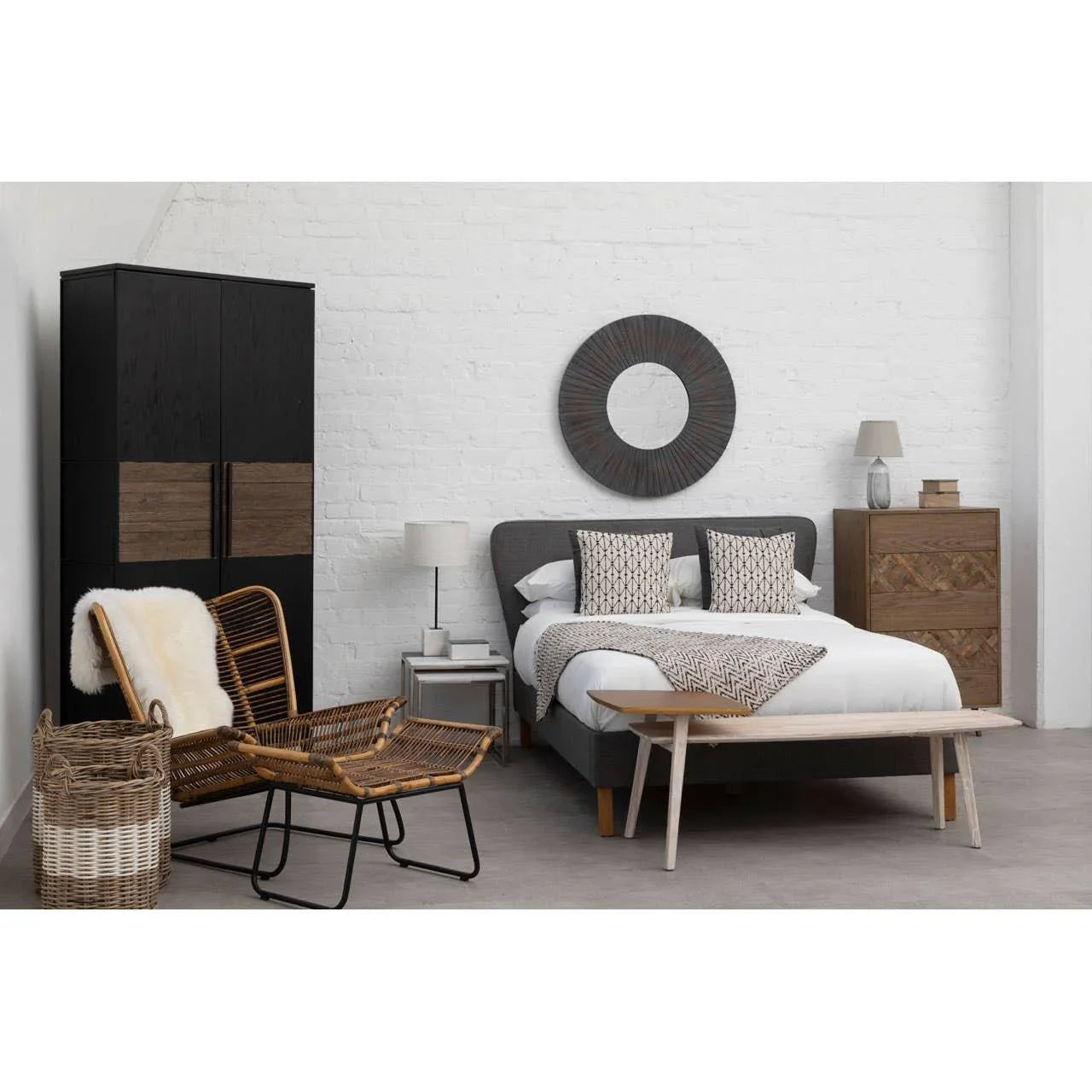 Modern bedroom with grey upholstered bed, geometric cushions, rattan chair, wooden wardrobe