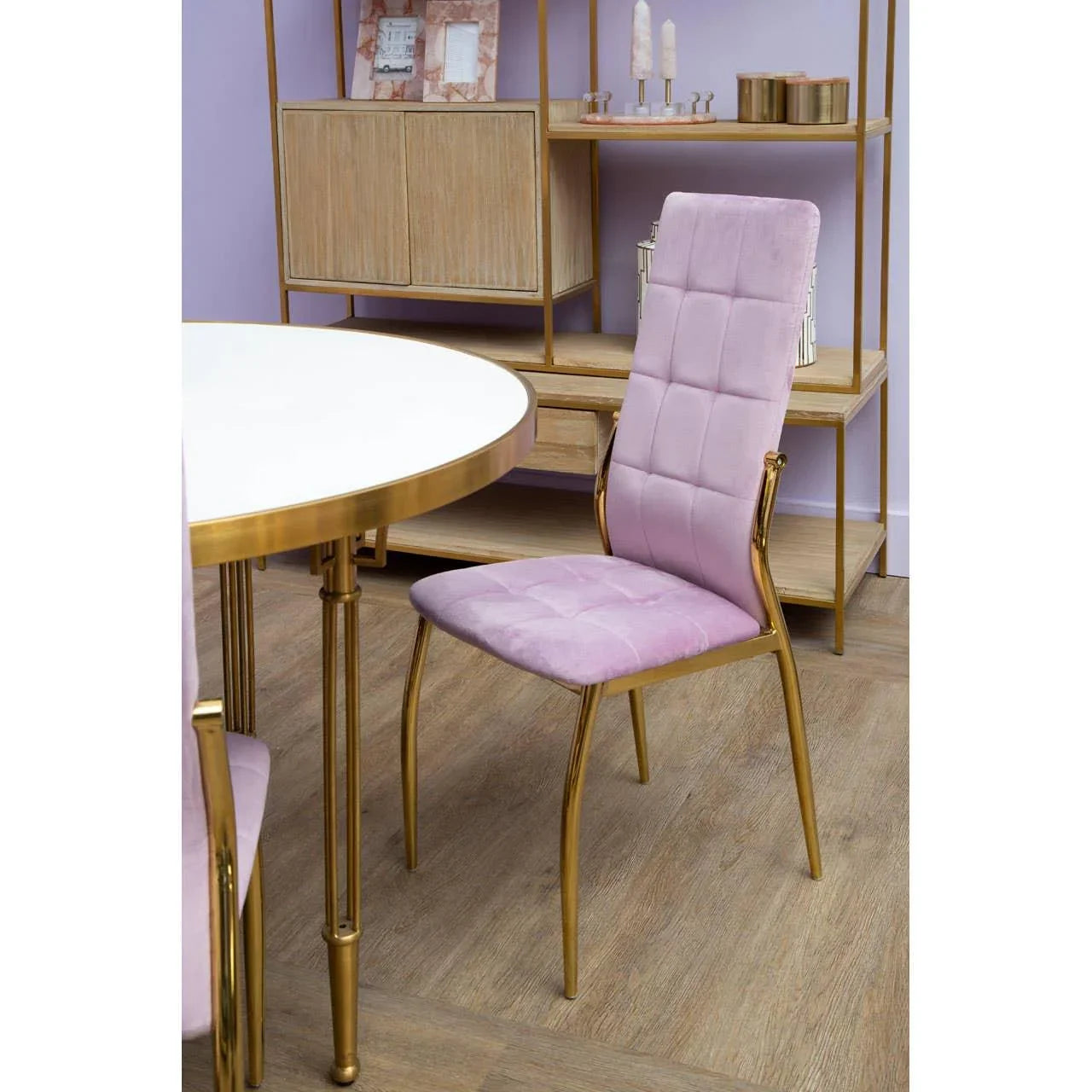 Pink velvet dining chair with gold metal frame beside round white and gold dining table