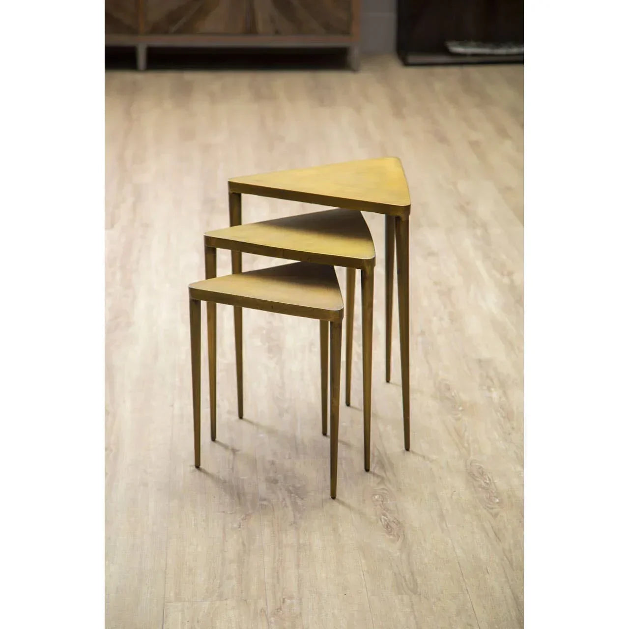 Set of three gold metal nesting tables with triangular tops on wood floor