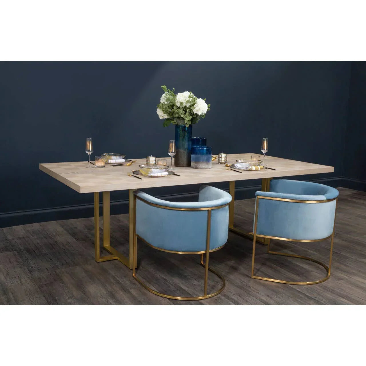 Modern dining table with light wood top, gold frame and two blue velvet dining chairs
