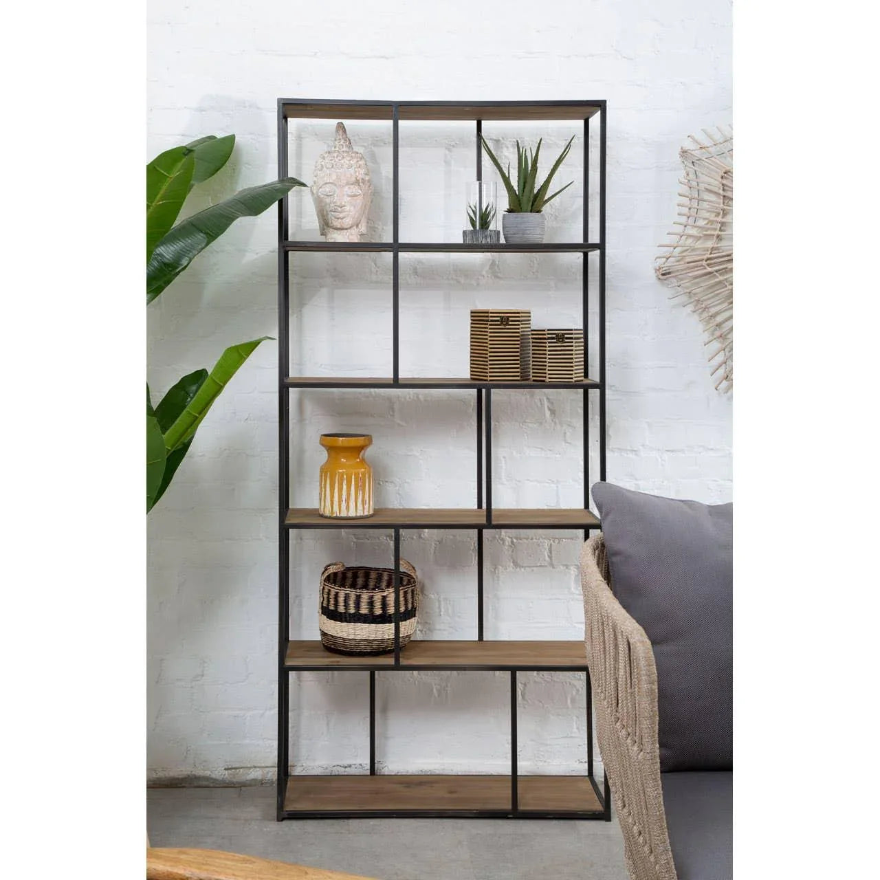 Black metal and wood shelving unit with decor items against white brick wall