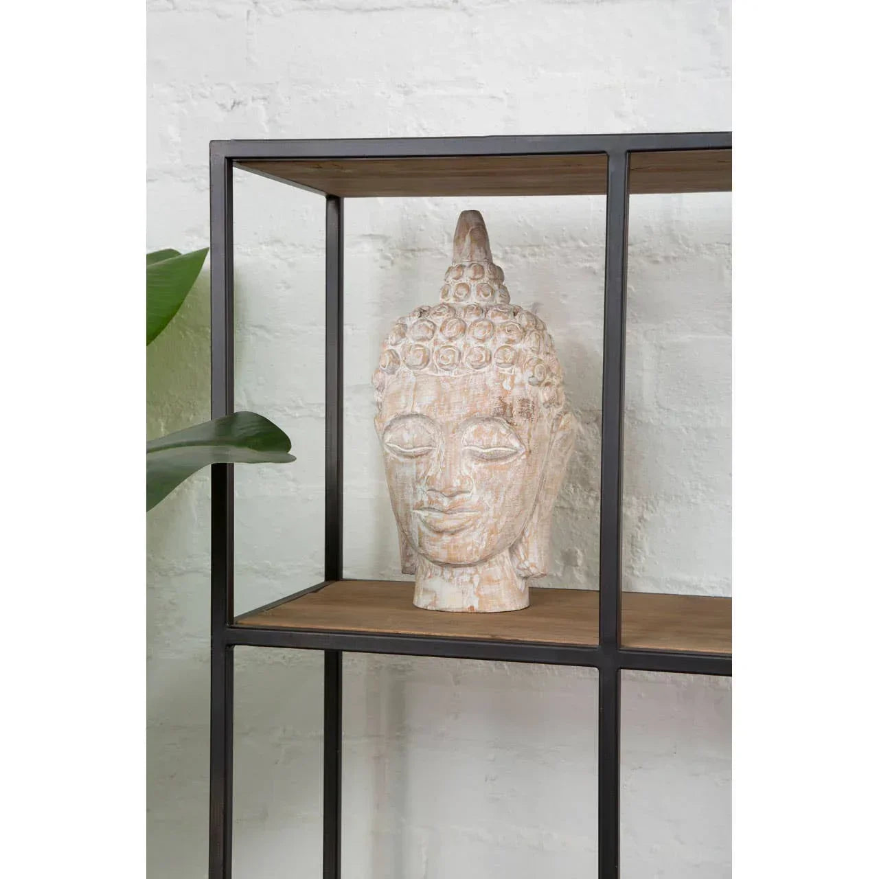 Carved Buddha head sculpture on metal and wood shelf against white brick wall