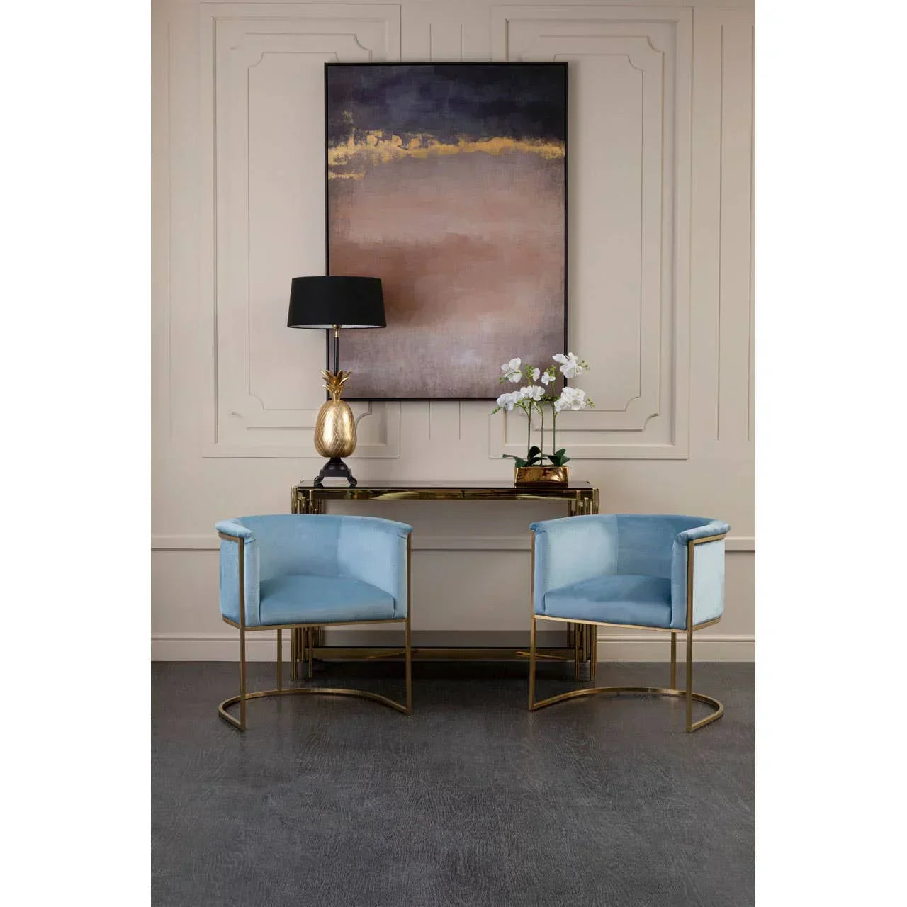 Blue velvet accent chairs with gold frames in front of console table and abstract wall art