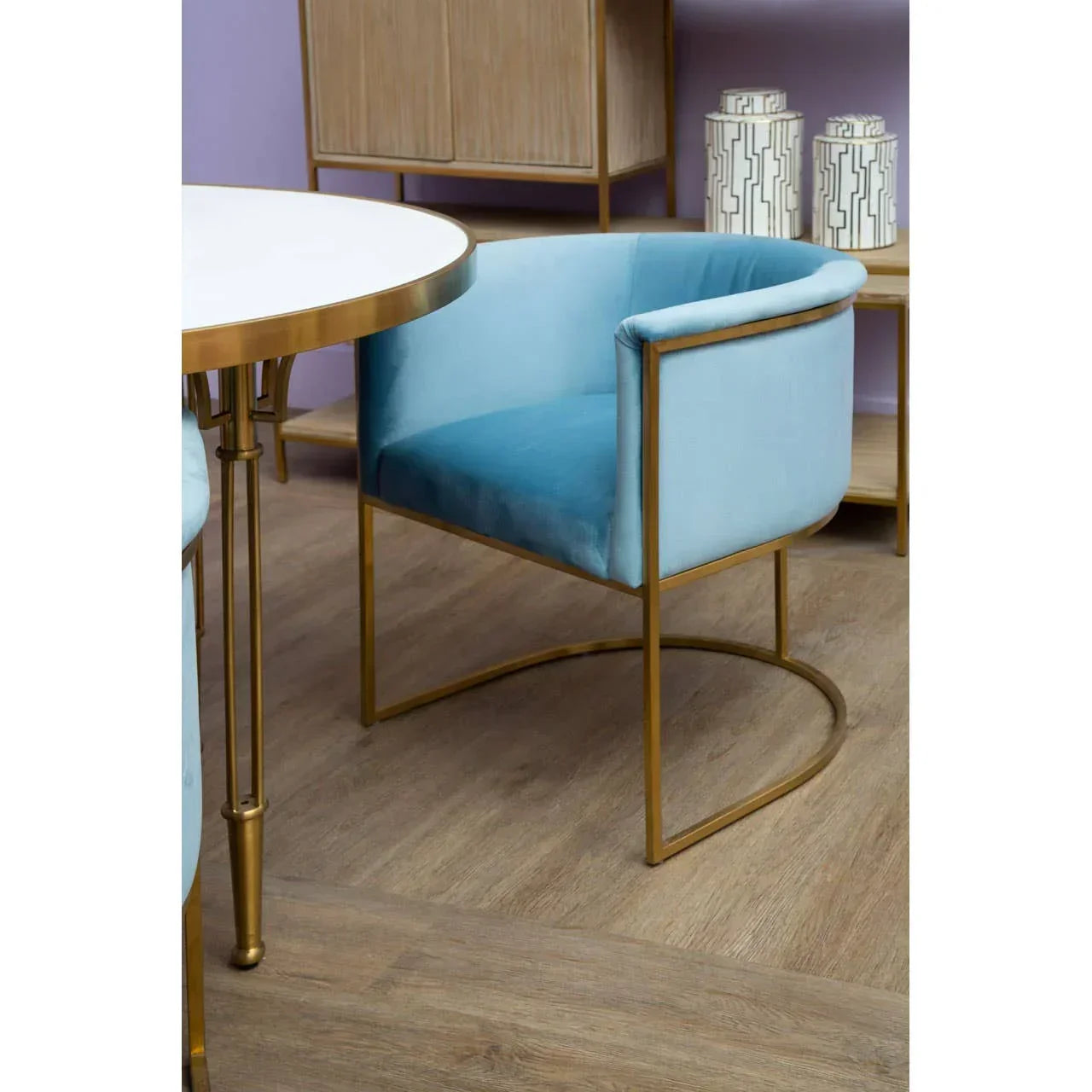 Blue velvet dining chair with gold metal frame beside round dining table