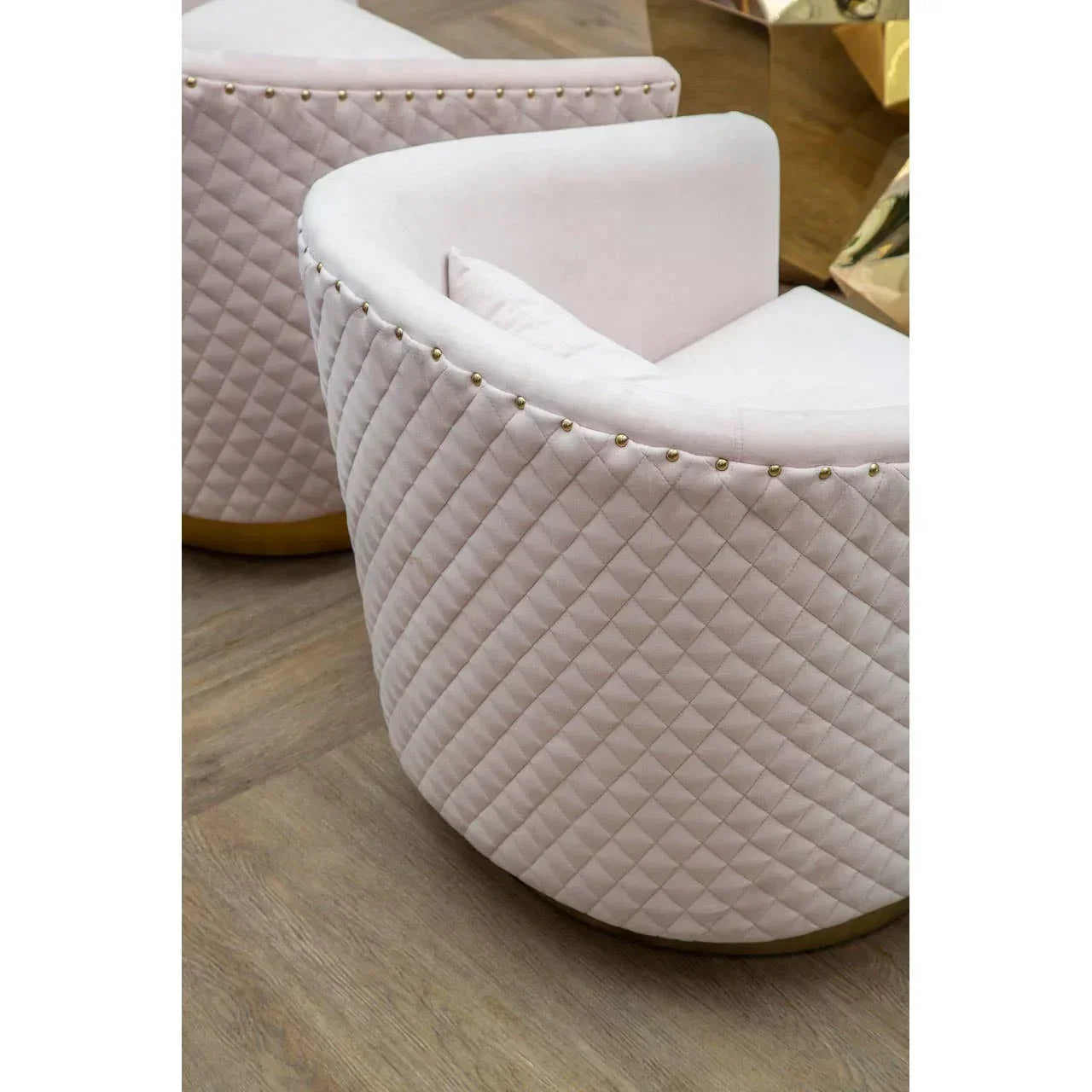 Blush pink accent chair with quilted velvet upholstery and gold stud detail on wooden floor