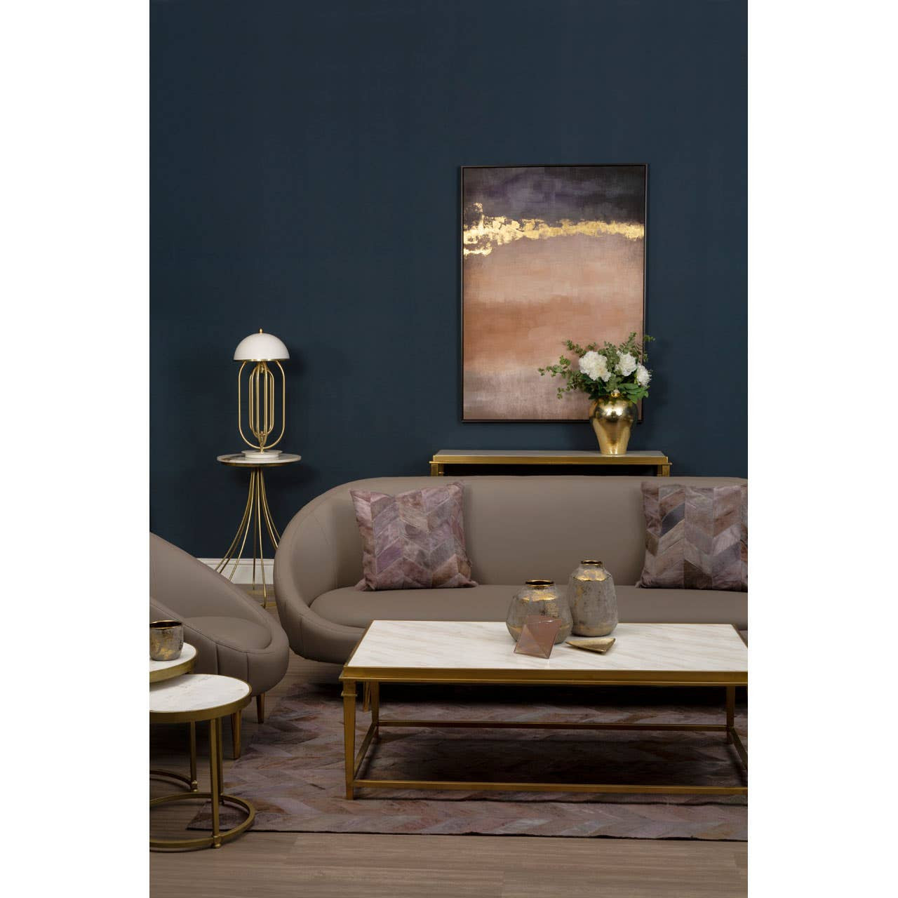 Brown leather effect 3 seater sofa with plush cushions, set against a dark blue wall. A stylish coffee table with decorative vases sits in front of the sofa, complemented by a modern lamp and a piece of wall art in the background