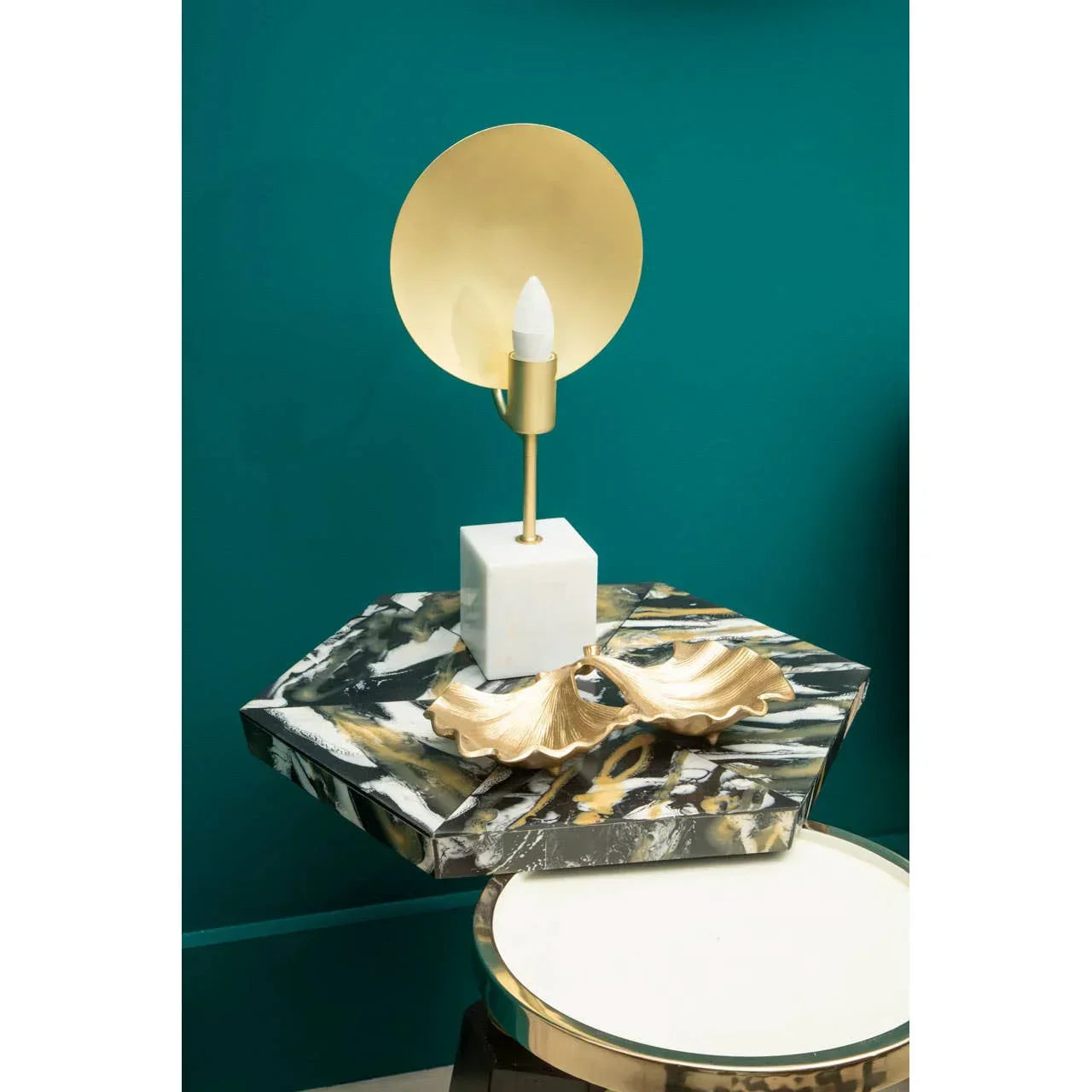 Gold and marble table lamp with sculpted tray on hexagonal marble side table against teal wall