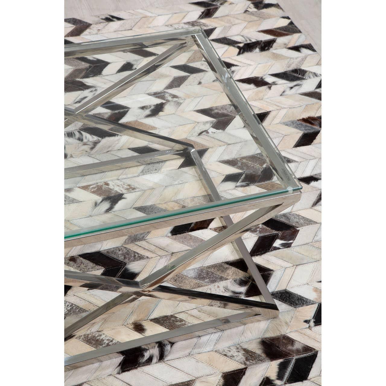 Glass coffee table with geometric chrome frame on patterned rug