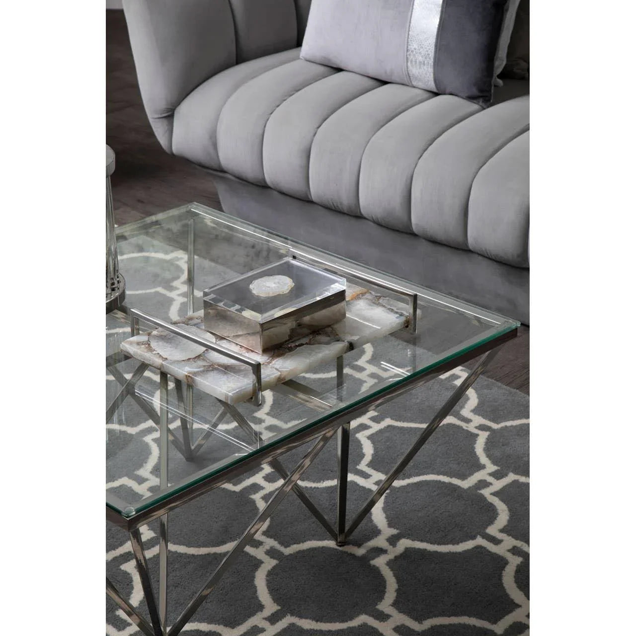 Glass coffee table with chrome legs and marble tray beside a grey velvet sofa on patterned rug