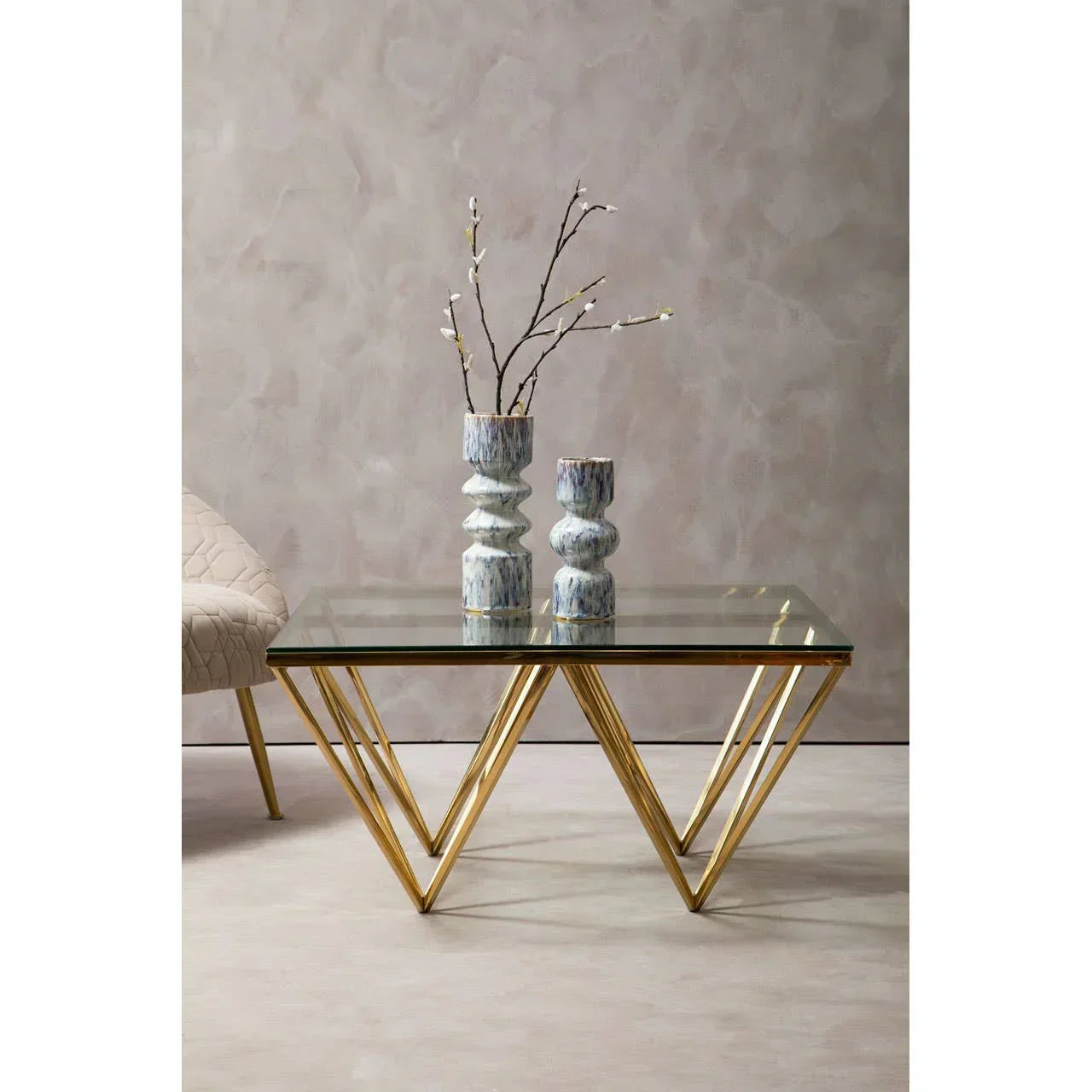 Glass coffee table with gold geometric legs and two ceramic vases in modern living room