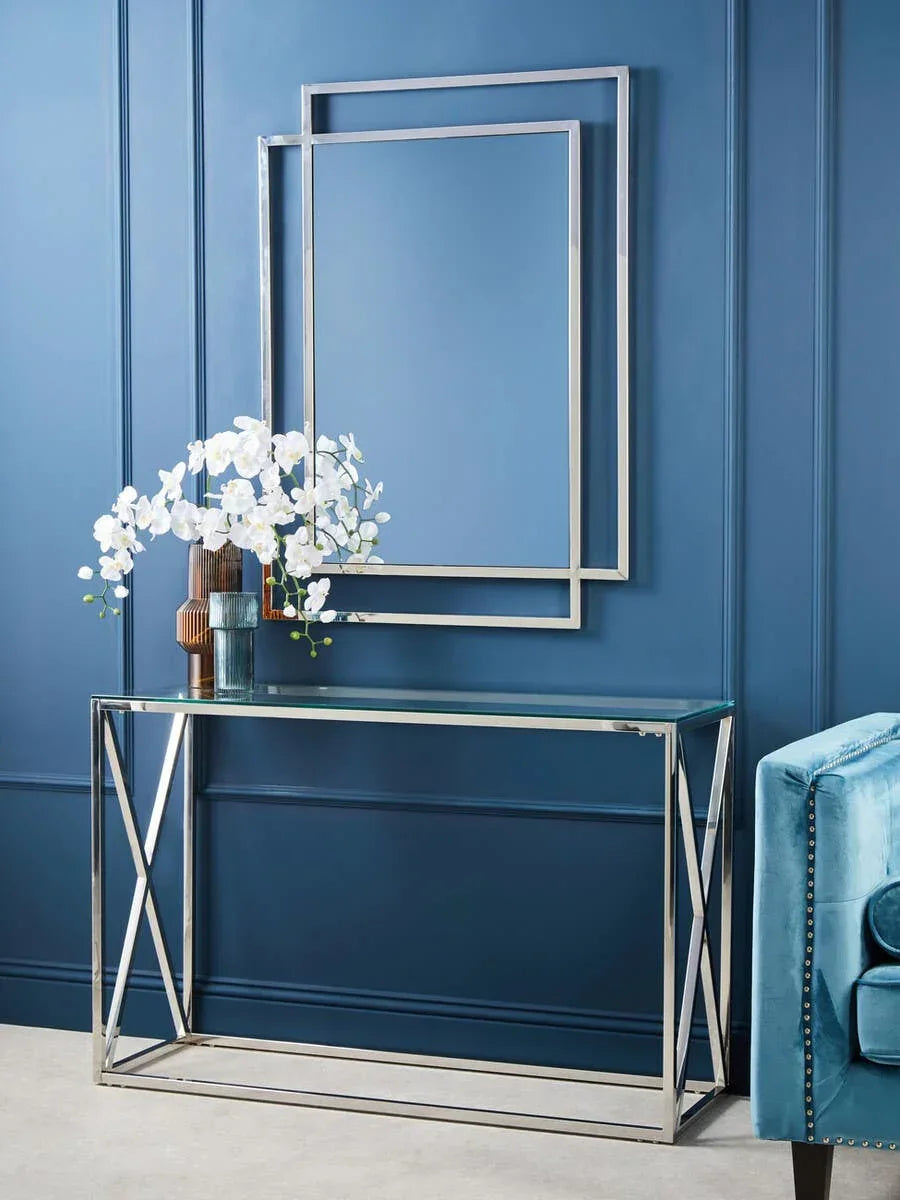 Glass console table with chrome frame beside blue accent chair and wall mirror