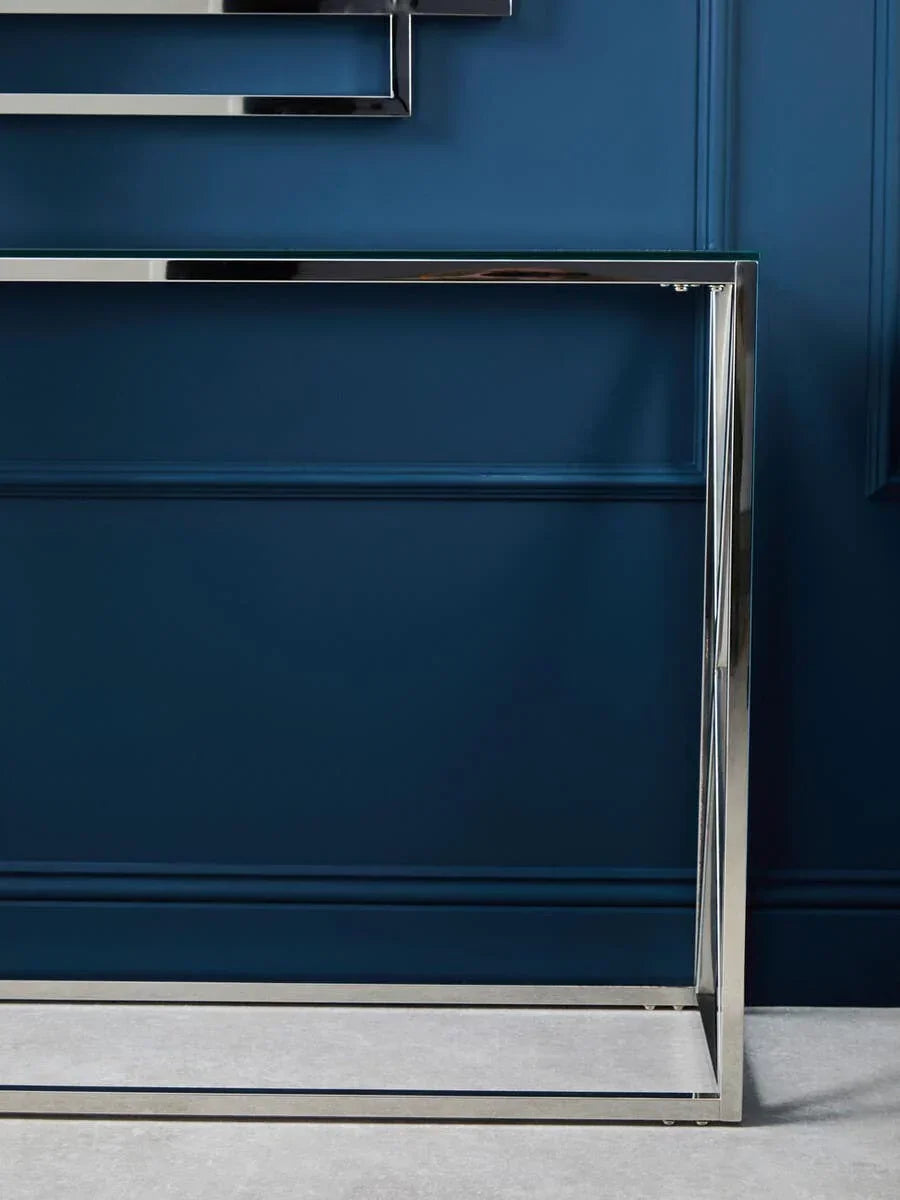 Chrome console table with glass top against a blue panelled wall on a grey floor