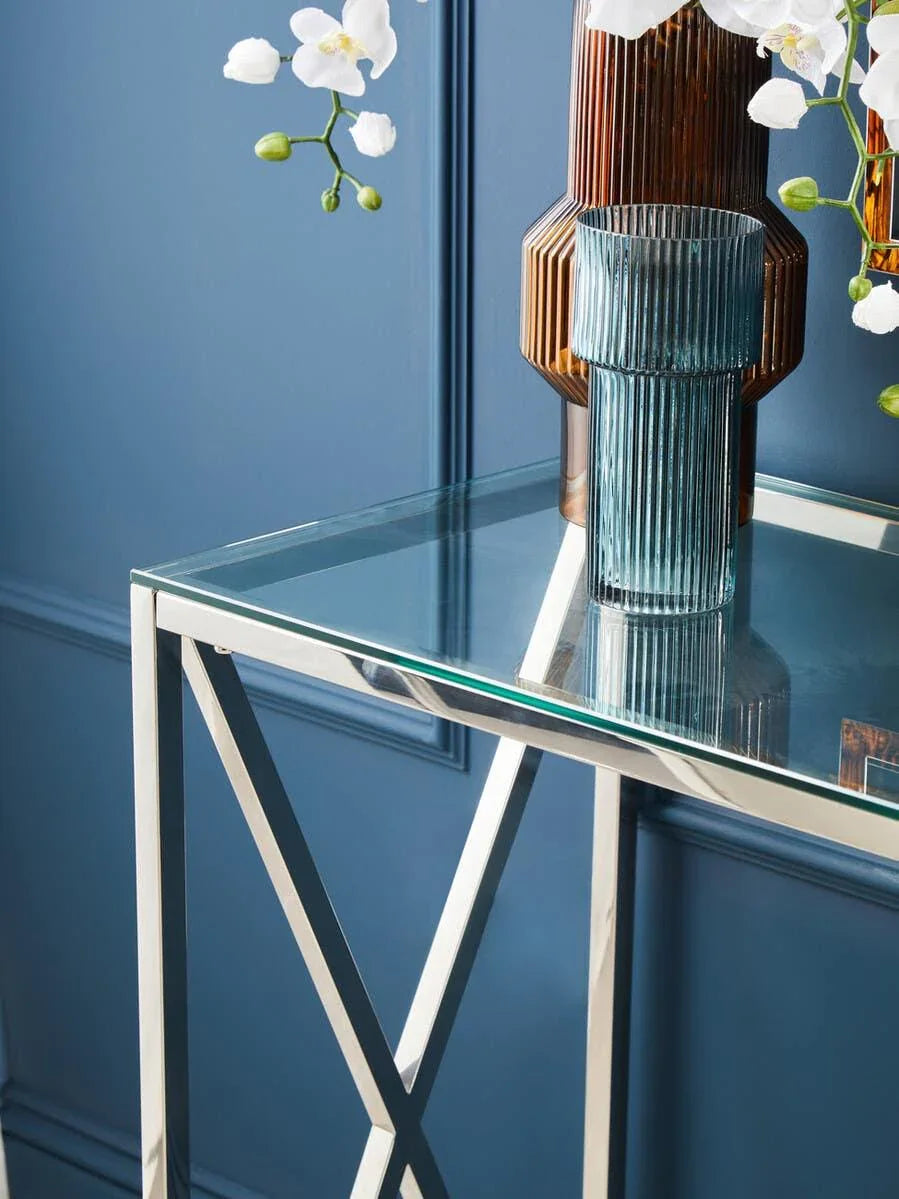 Glass console table with chrome legs beside blue wall, vases and white orchids on top