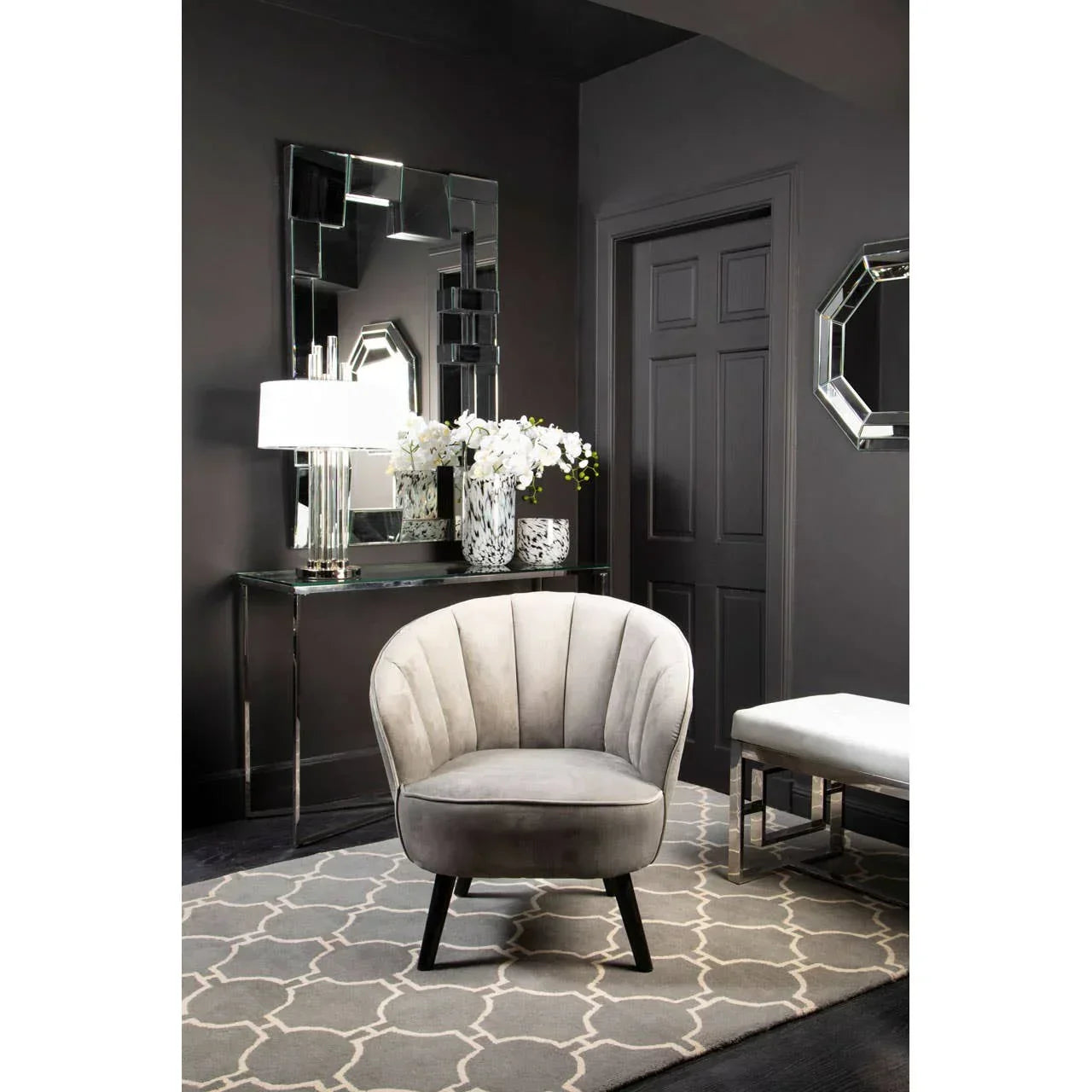 Grey velvet accent chair with black legs in a modern entryway on patterned rug
