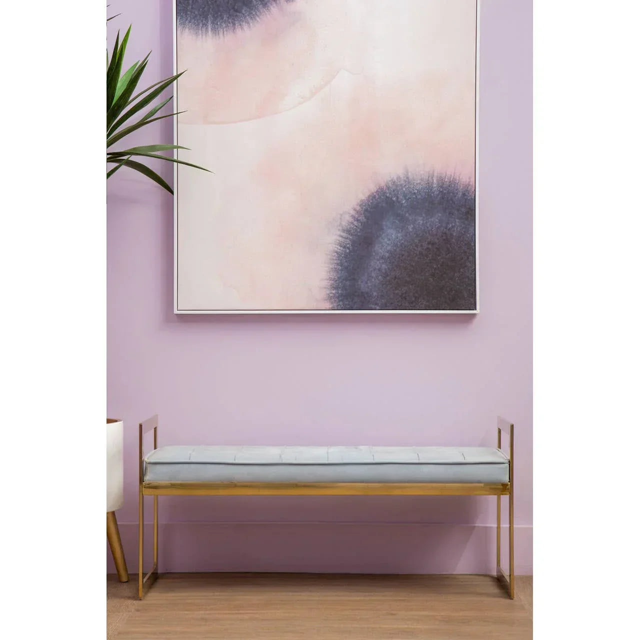 Velvet bench seat with gold metal frame set against light purple wall and abstract artwork