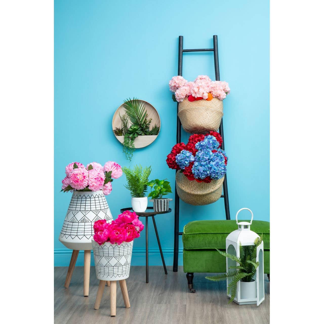 Artificial flowers in decorative planters and baskets beside green upholstered bench on blue wall