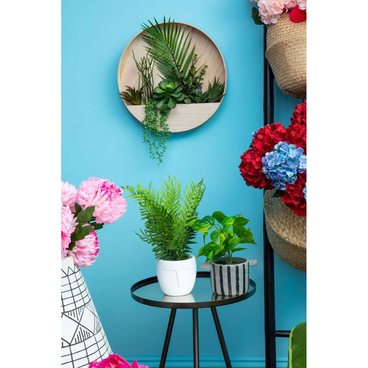 Indoor plant display with potted artificial foliage and wall-mounted planter on glass table