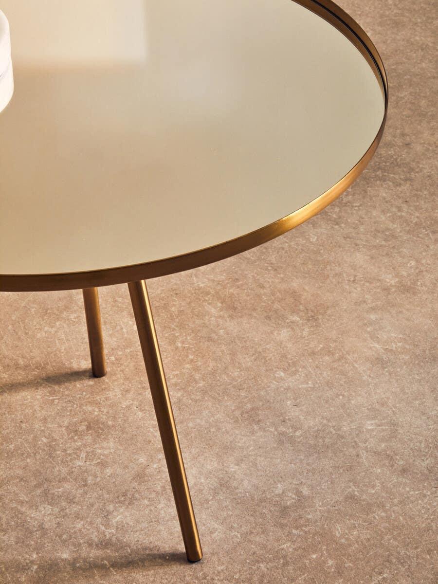 Round glass coffee table with gold metal frame and legs on stone floor