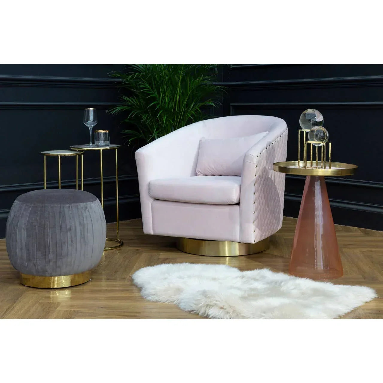 Blush velvet accent chair with gold base beside round side table and grey footstool