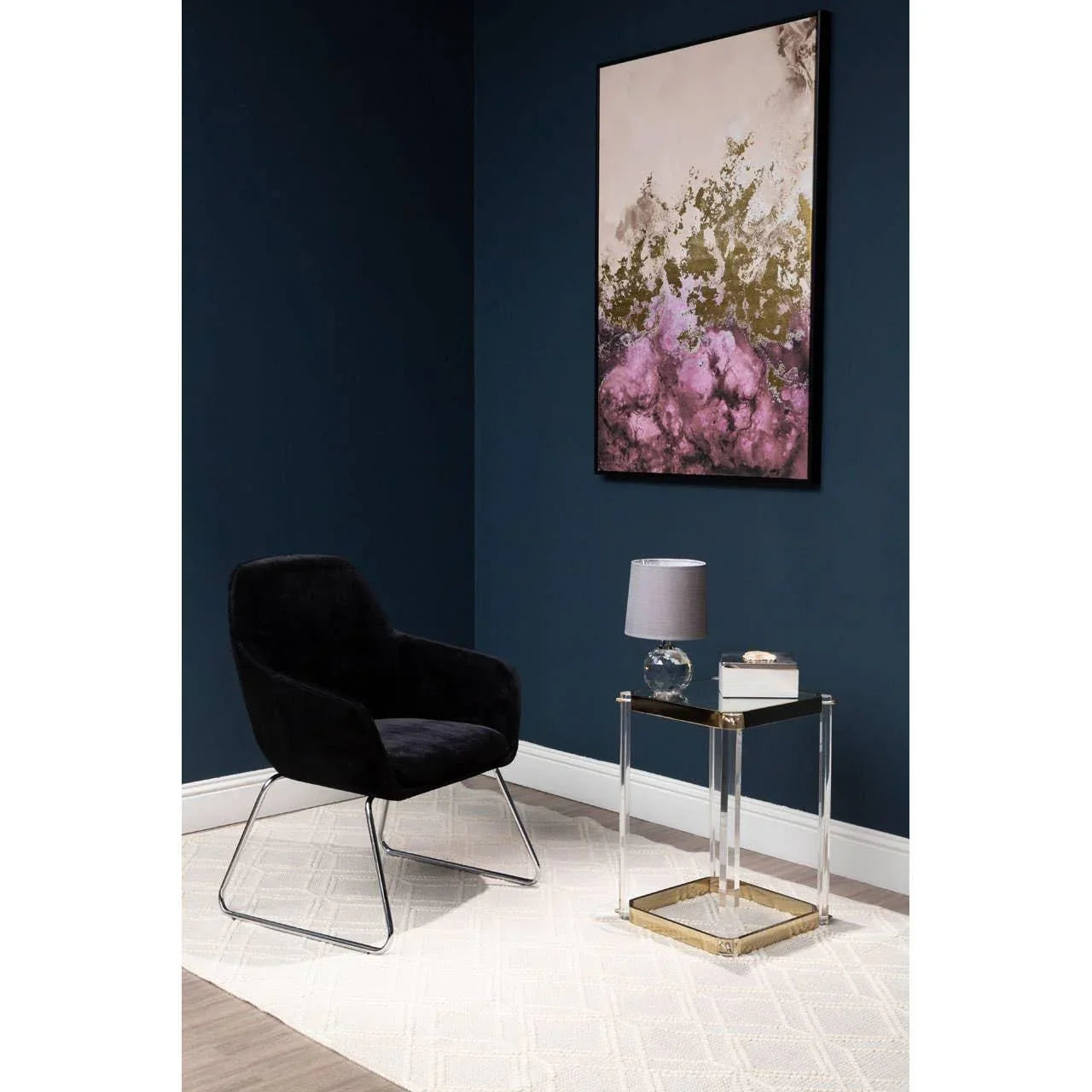 Black velvet accent chair with chrome legs next to glass side table and modern table lamp