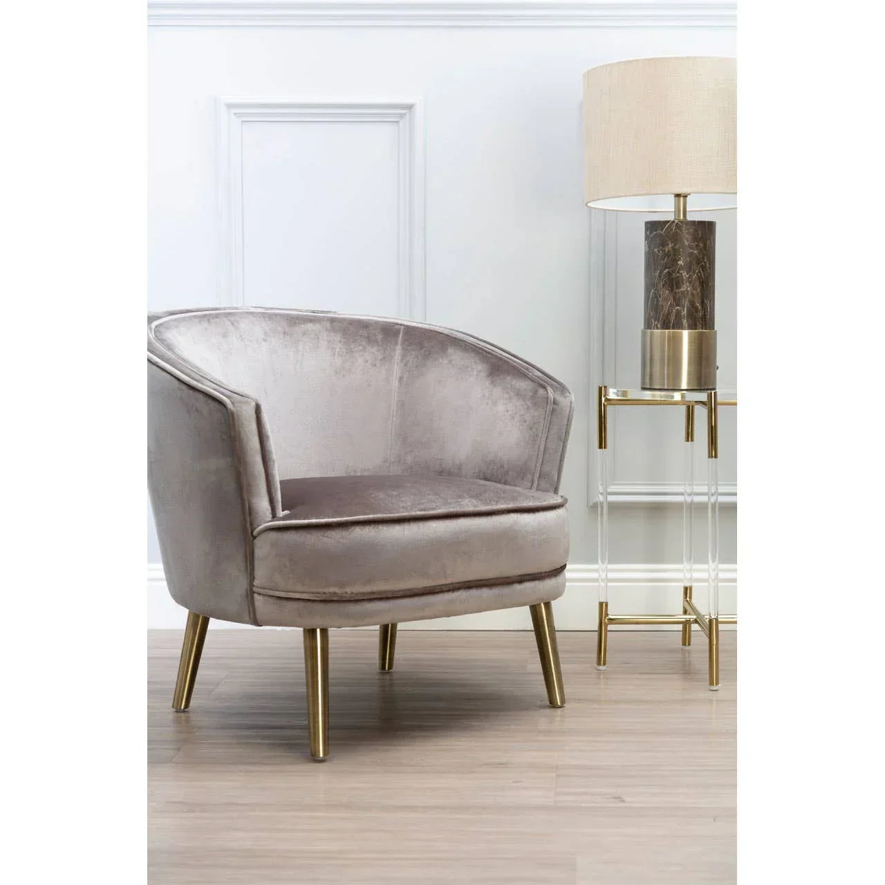 Velvet accent chair with gold legs beside marble table lamp on acrylic side table