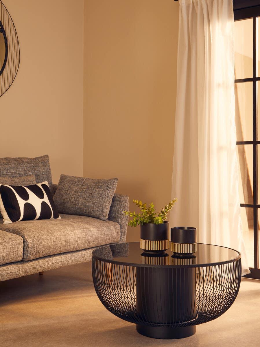 Modern black wire coffee table with glass top beside grey sofa in living room