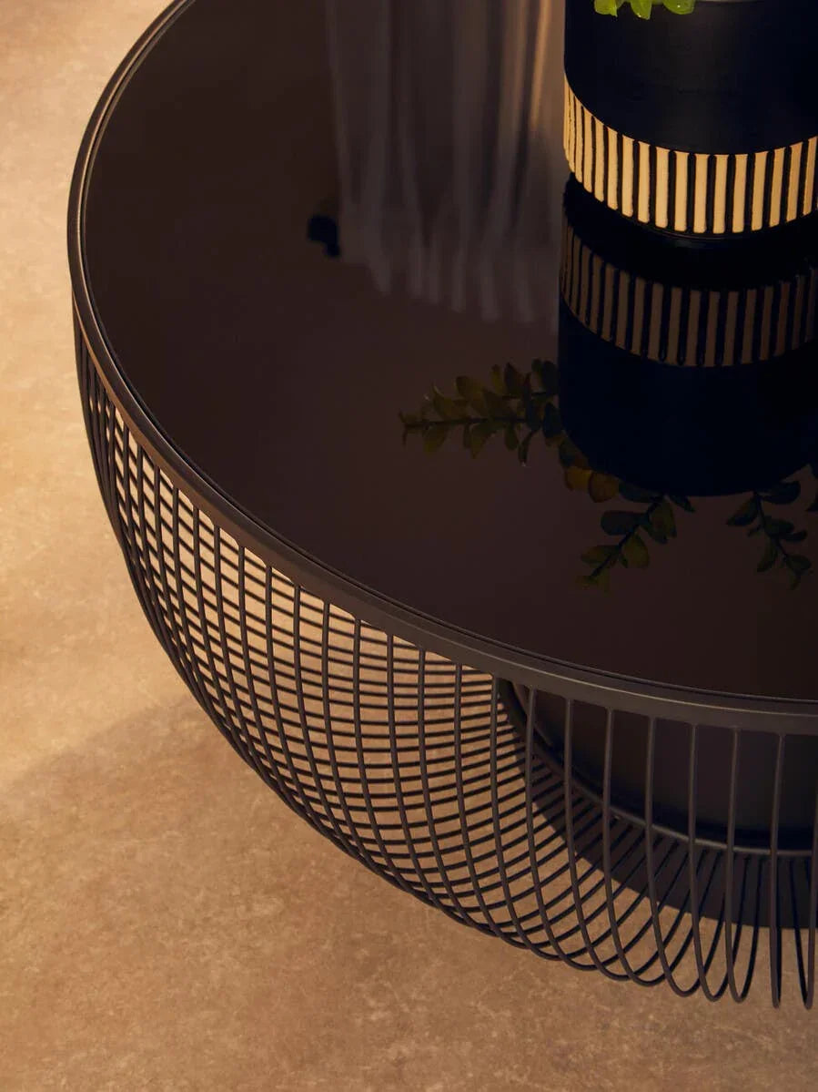 Round black wire frame coffee table with glass top and decorative vase detail