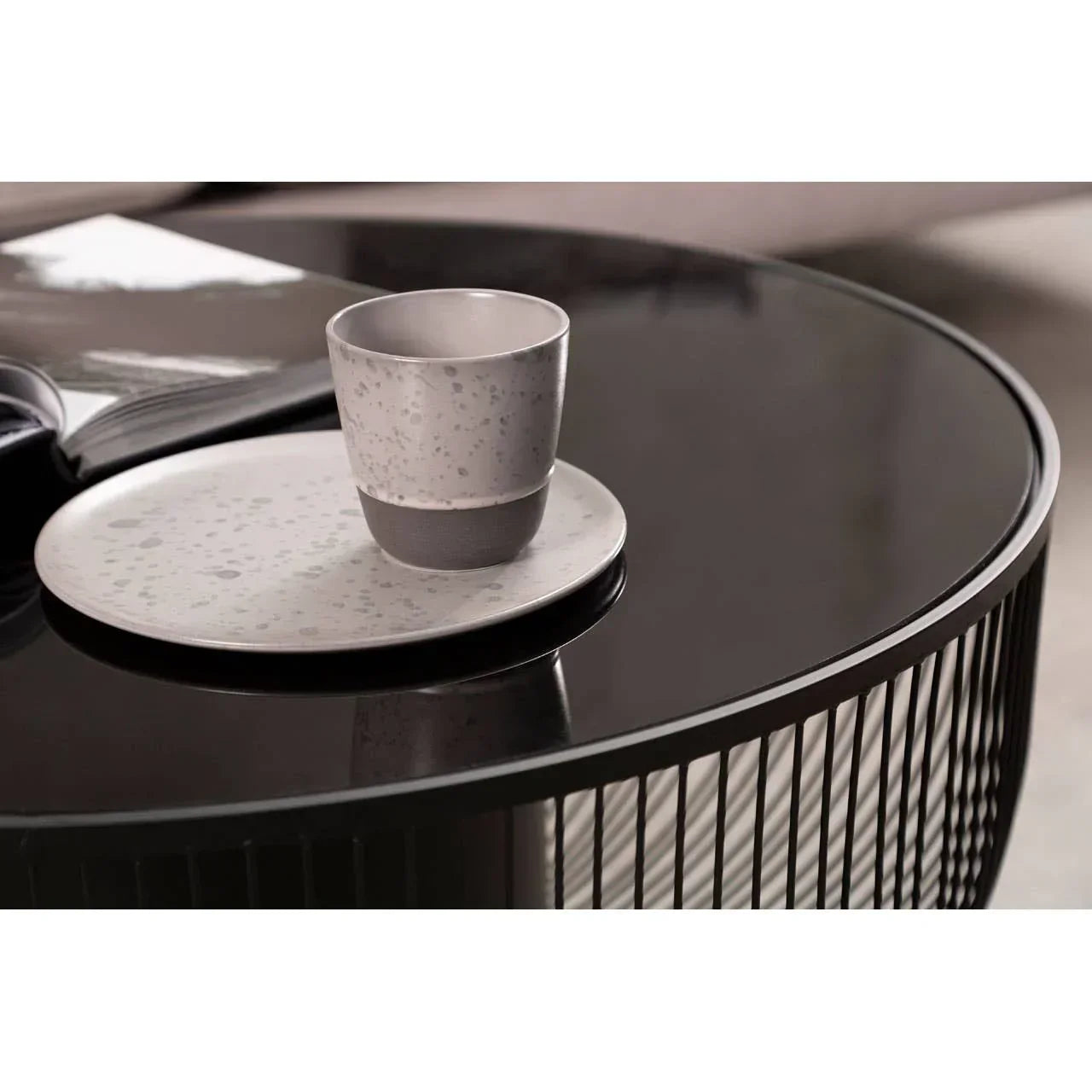 Modern black coffee table with ceramic cup and plate, open book in background