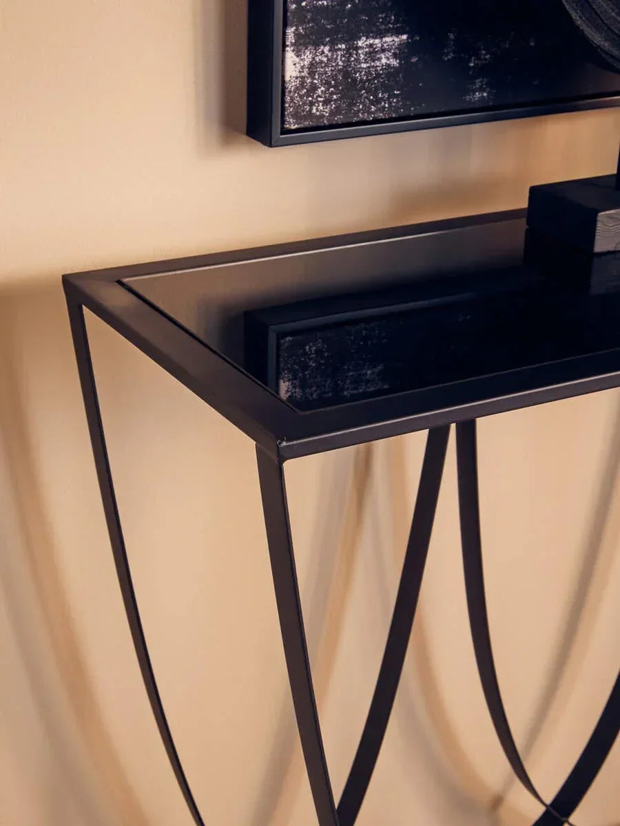Black glass console table with curved metal legs against beige wall
