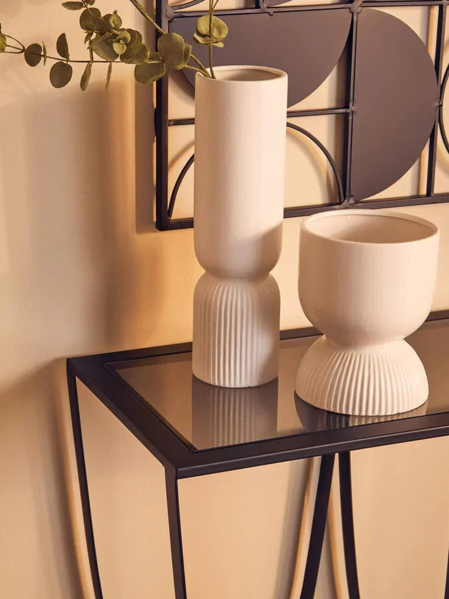 Modern ceramic vases on glass console table with metal frame against cream wall