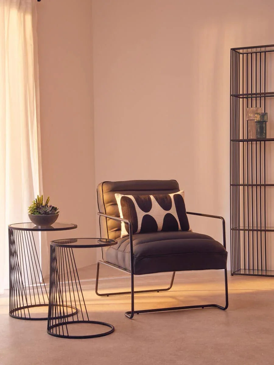 Black leather accent chair with metal frame, glass side tables, and geometric cushion