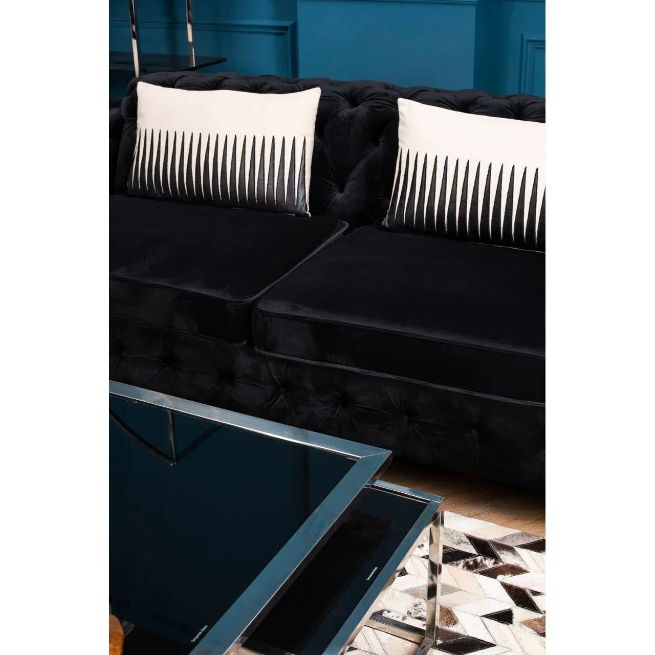 Black velvet sofa with tufted cushions and monochrome accent pillows beside glass coffee table