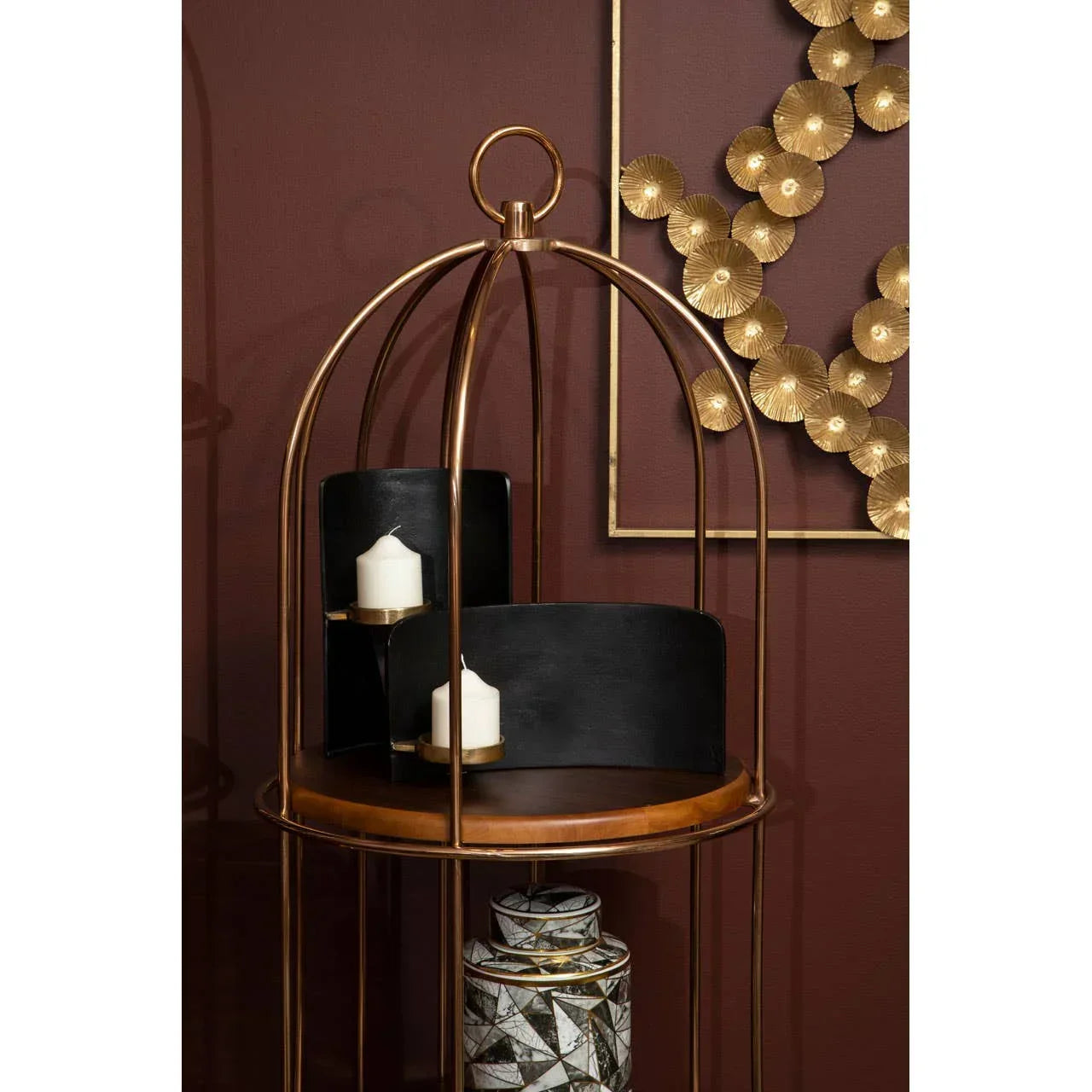 Gold metal side table with decorative candles and geometric storage jar against dark red wall