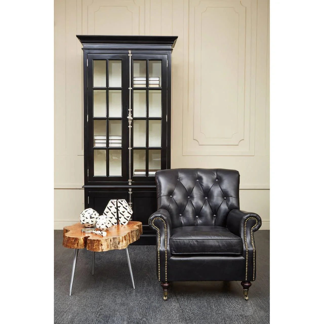 Black leather armchair with nailhead trim beside wooden side table and glass display cabinet