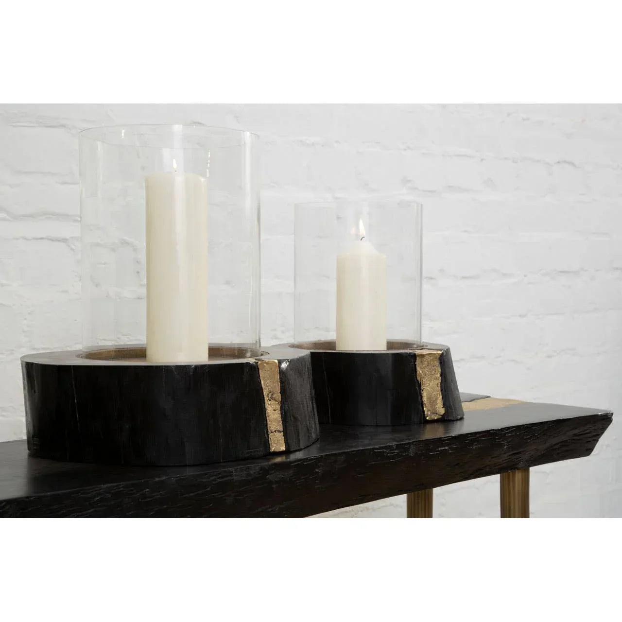 Pair of pillar candles in glass hurricane holders with black wood and gold trim bases on table
