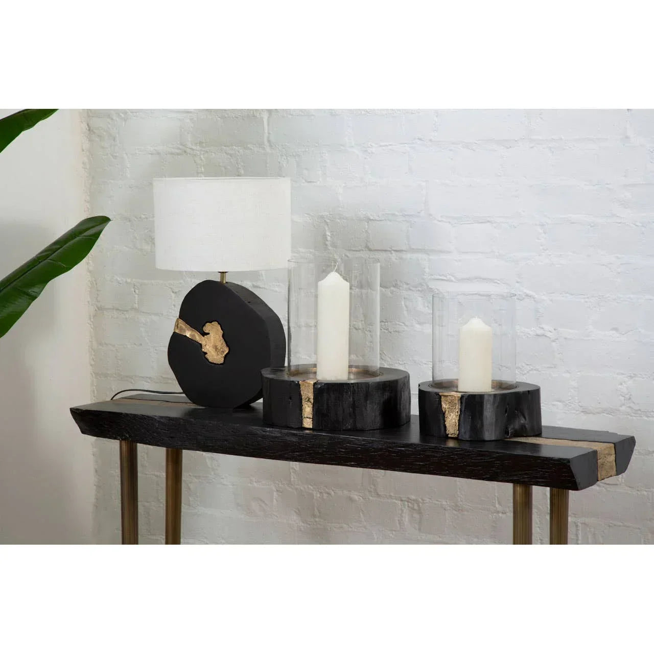 Black wood console table with gold accents, lamp, and two pillar candle holders