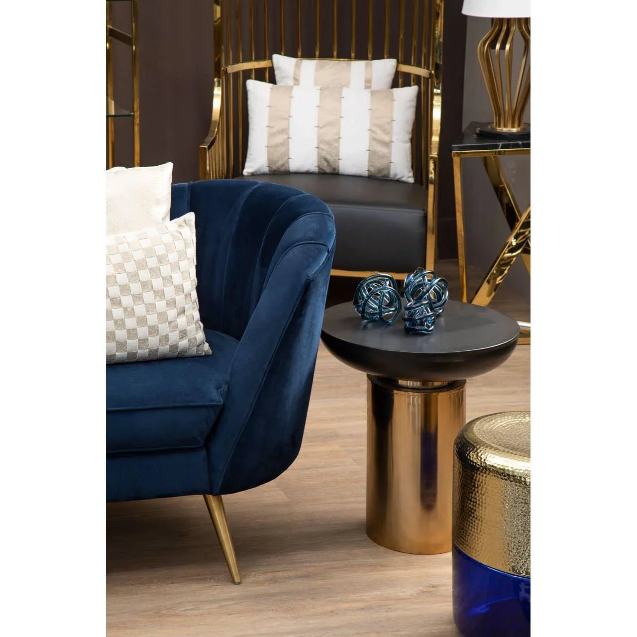 Navy blue velvet sofa with gold legs beside round gold side table in modern living room