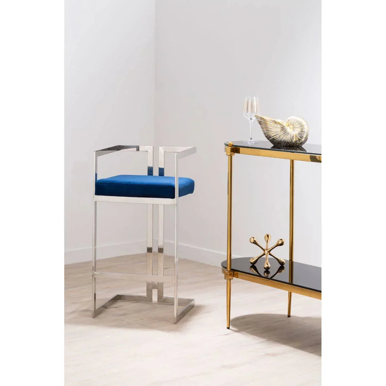 Modern bar stool with chrome frame and blue cushion beside gold console table