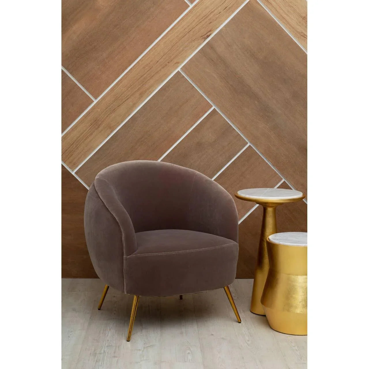 Velvet armchair with gold legs next to gold side tables on wood flooring