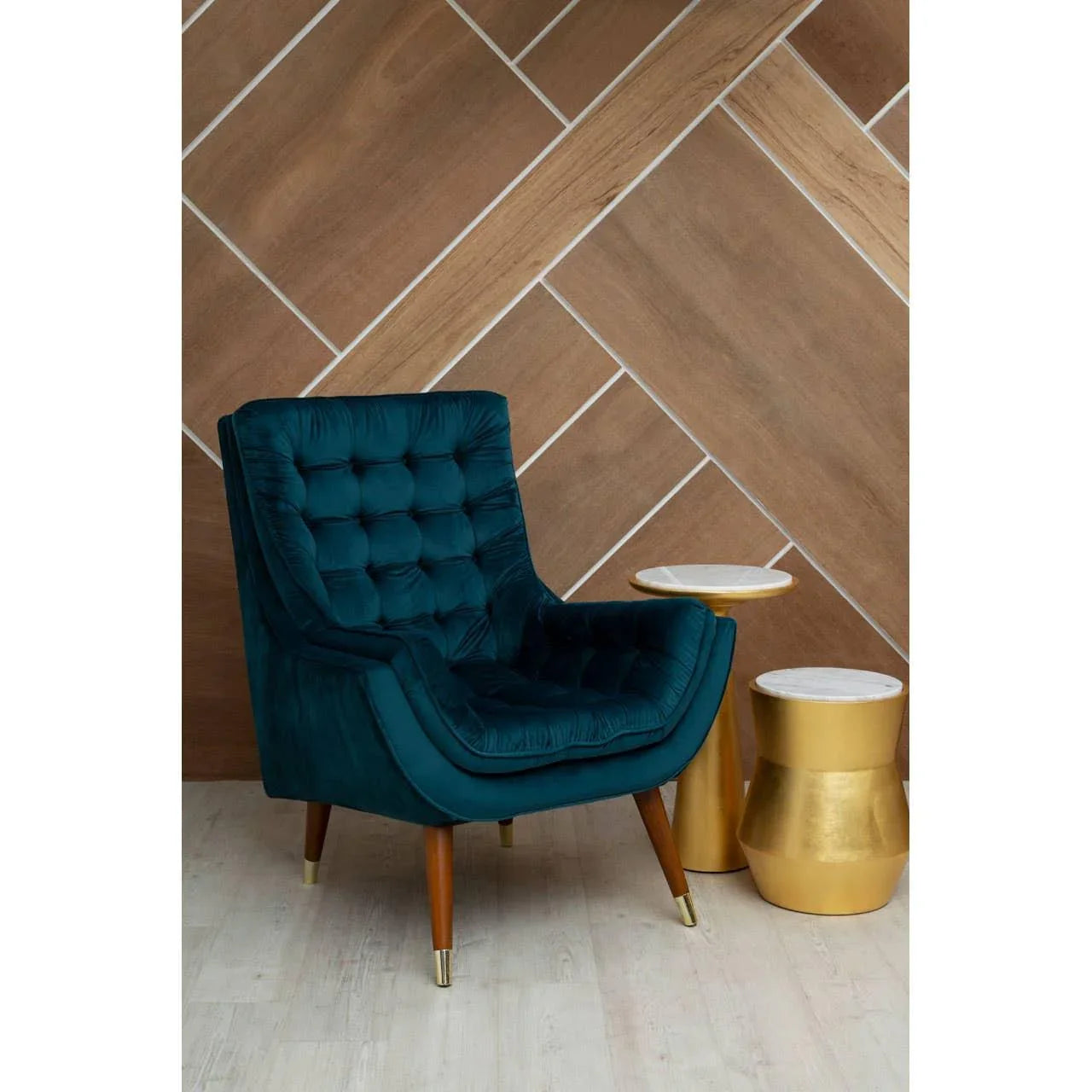 Teal velvet accent chair with wooden legs beside two gold and marble side tables