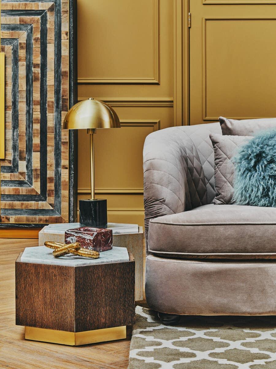 Beige velvet sofa with blue cushion, hexagon wood side tables, gold lamp in living room