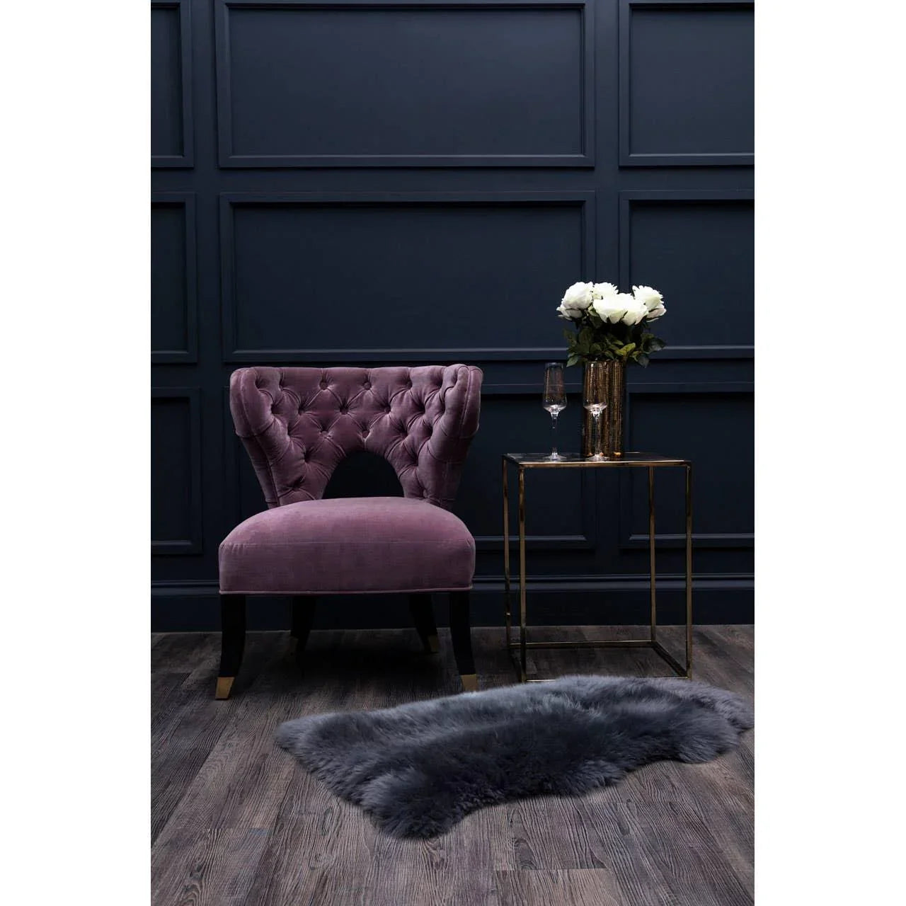 Plum velvet accent chair with button back next to gold side table and faux fur rug on wood floor