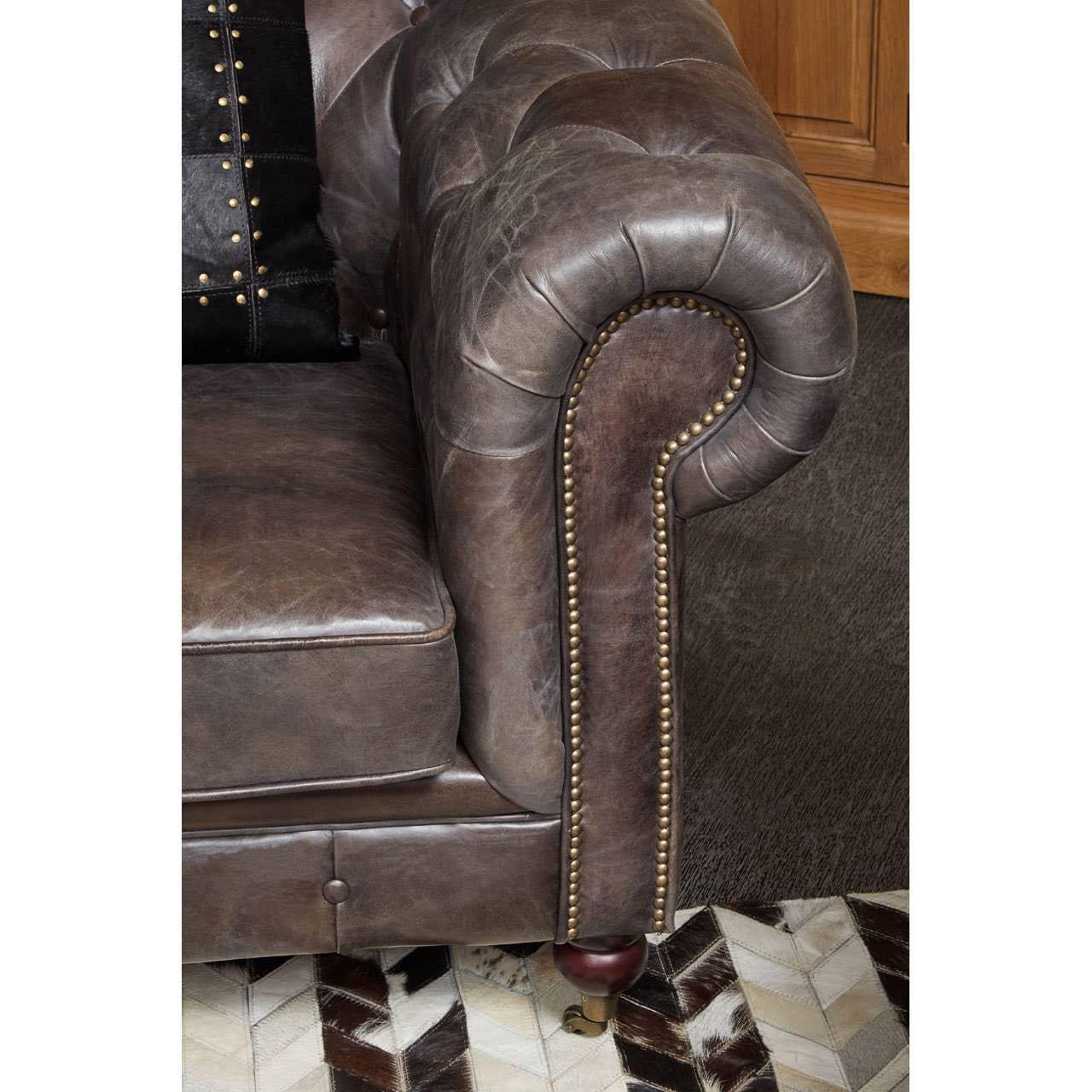Brown leather sofa arm with button detailing and brass studs on patterned rug